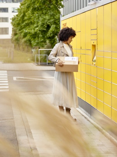 Frau steht mit Paket vor DHL Packstation
