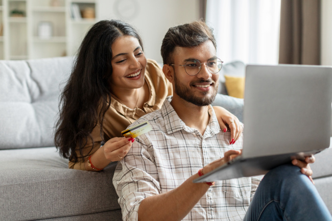 Indisches Paar auf der Couch guckt fröhlich auf Laptop