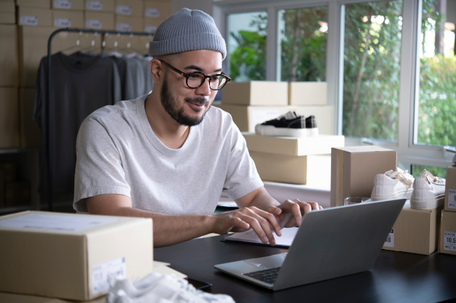 Junger Mann zwischen Kisten schreibt am Laptop